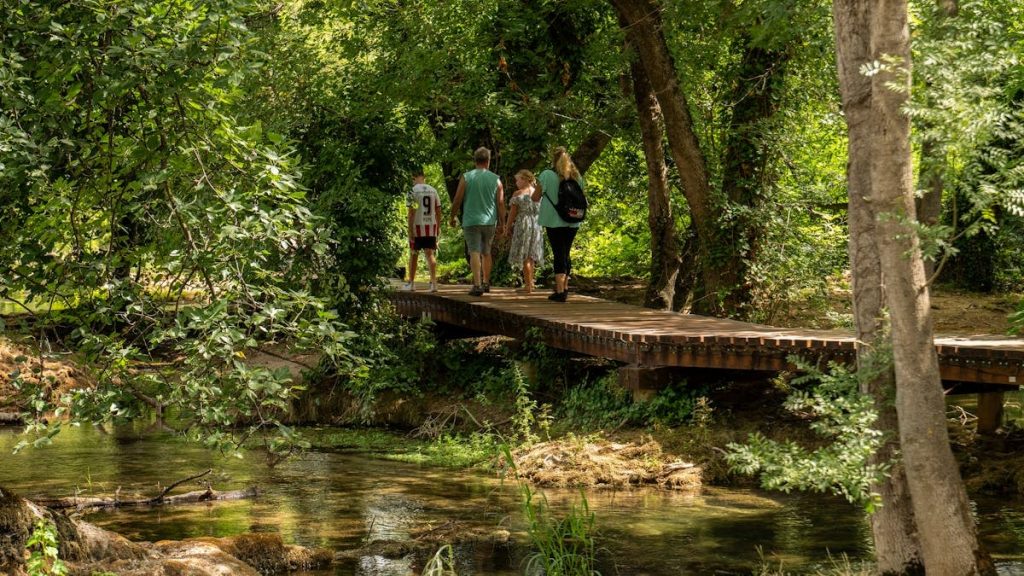 A family strolls across a wooden bridge in a lush Croatian forest, reflecting summer outdoor adventure.